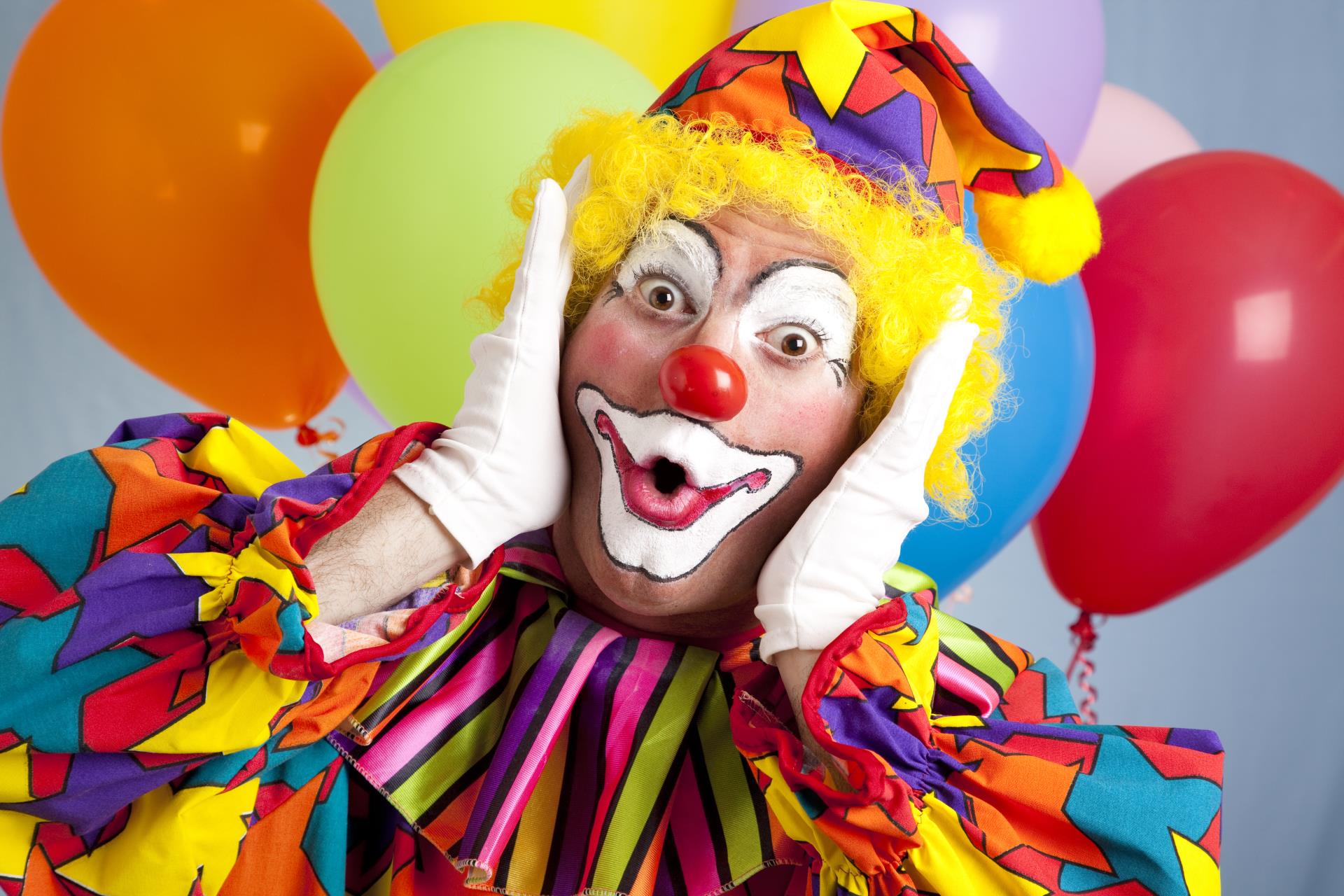 Colorful male clown standing in front of balloons