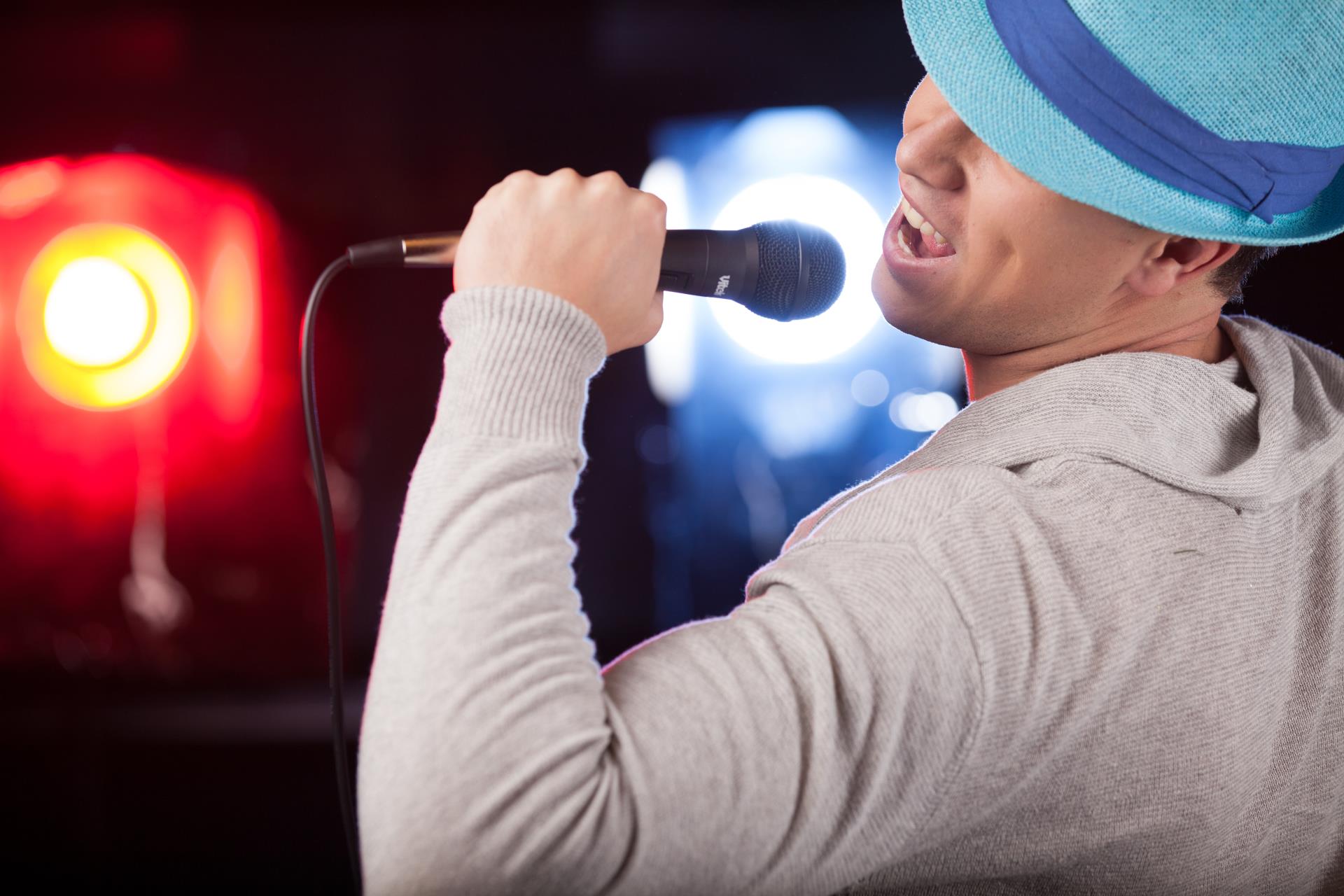 man singing into microphone with blue fedora